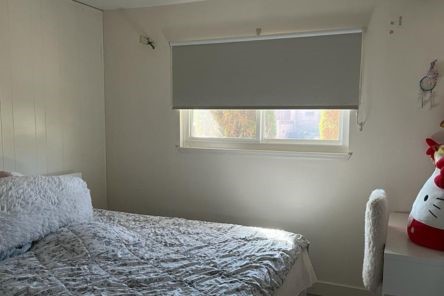 Sleek custom roller shades fitted over a large bedroom window with soft daylight filtering through.